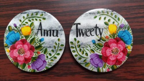 Fridge Magnet with flowers, same leaves and name on it along with white and black stony background.