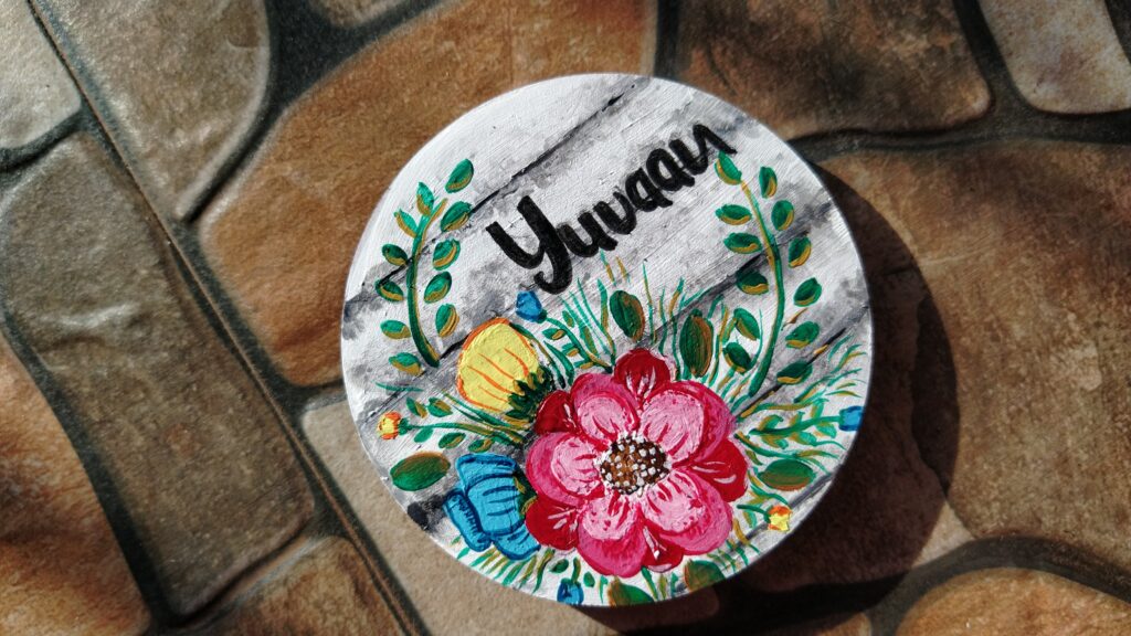 Fridge Magnet with flowers, same leaves and name on it along with white and black stony background.