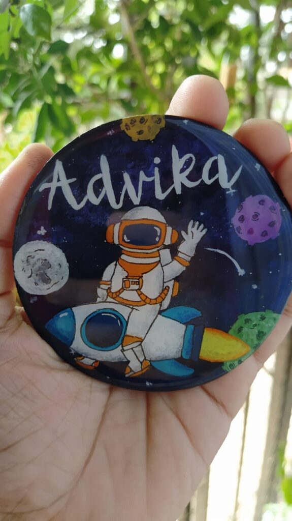 An astronaut cartoon sitting on the rocket with kid's name written on the fridge Magnet